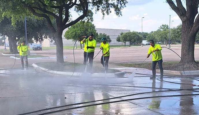 A team of four professional power washing a large concrete parking lot