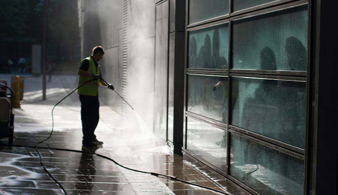 Worker power washing the walkway and glass entryway of a commercial building