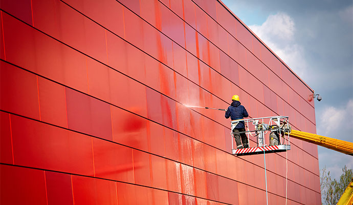 Person using a pressure washer to clean the exterior facade of a building
