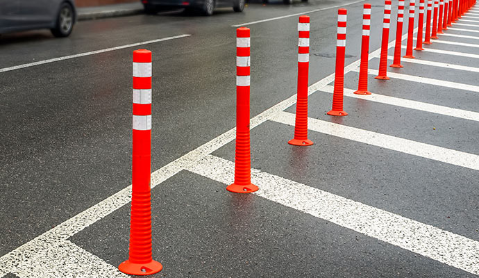 Flexible orange traffic delineator posts installed along roadway lane and pedestrian crossing area