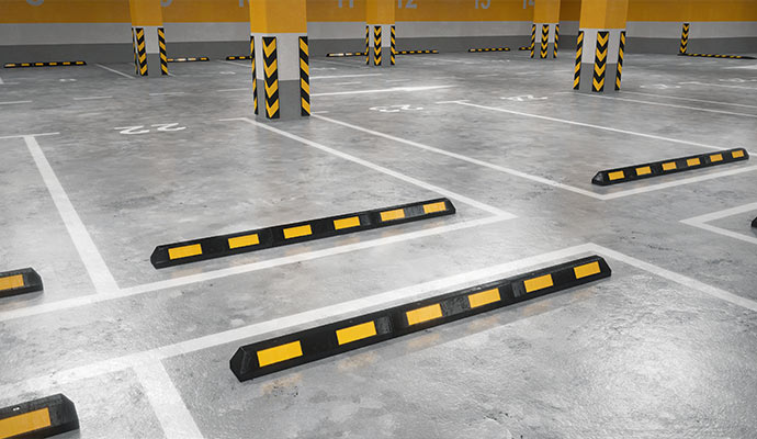 Indoor parking garage with rubber wheel stops marked parking spaces and safety striped support columns
