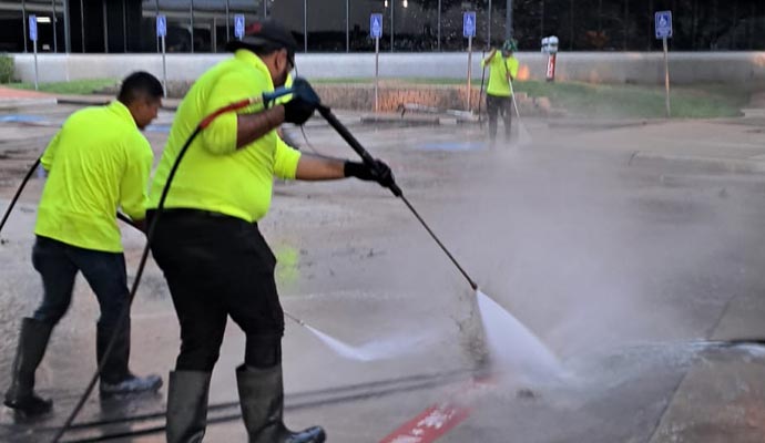 Commercial cleaning crew of three people are pressure washing a parking lot surface