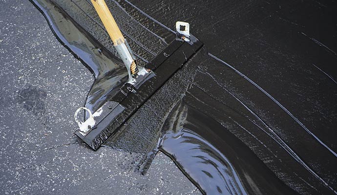 Professional squeegee applying a thick, black liquid sealcoat to a driveway
