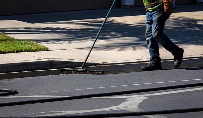 Using a long-handled squeegee applying sealcoat to a driveway