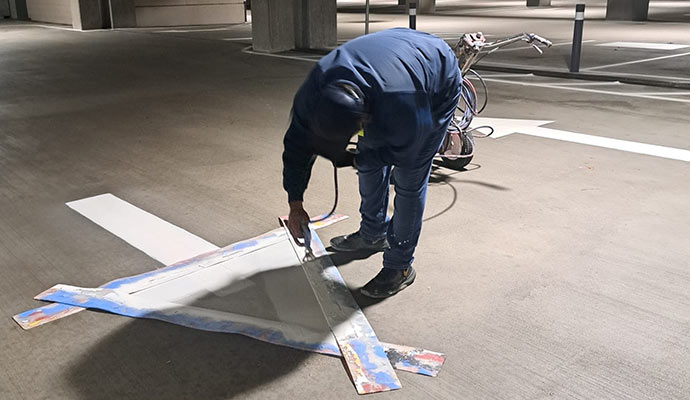 Professional contractor applying parking lot line striping and directional pavement markings in parking garage