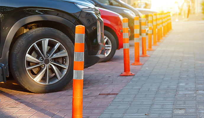 Orange reflective parking lot safety bollards installed beside parked vehicles along pedestrian walkway