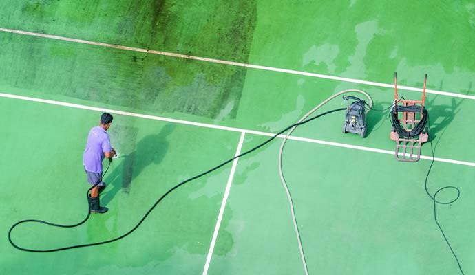 Technician power washing a dirty green tennis court surface