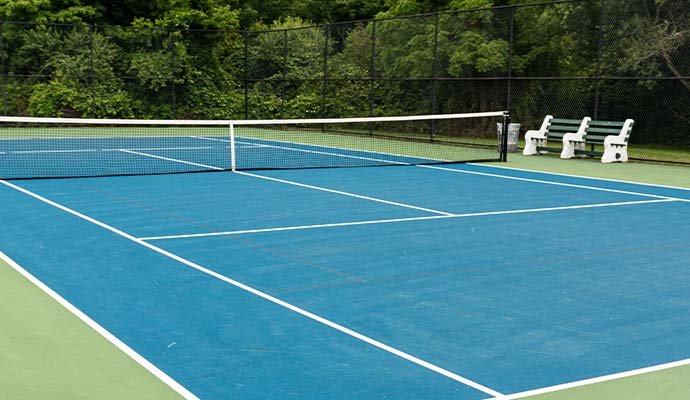Blue outdoor tennis court with benches and trees in the background