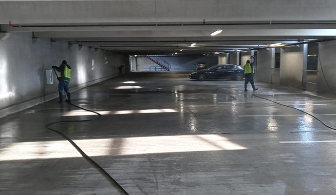 Two professionals are power washing concrete garage