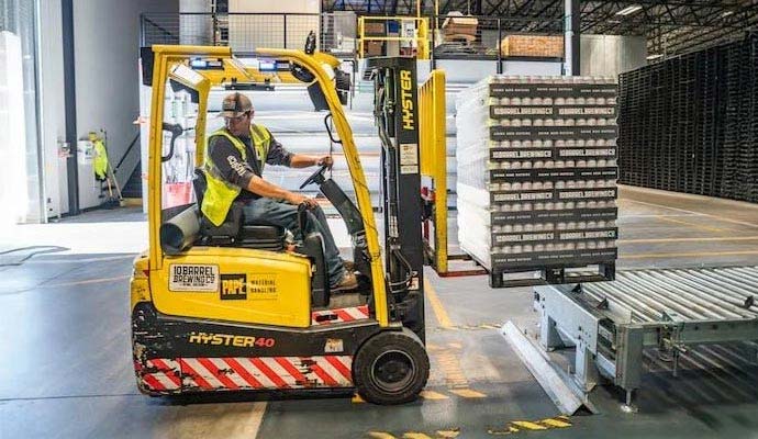 Forklift driver moving inventory in a warehouse with yellow floor safety markings