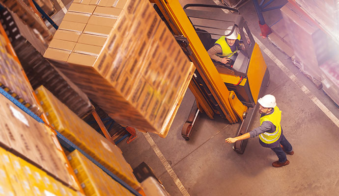 Two warehouse workers moving large boxes in a storage facility